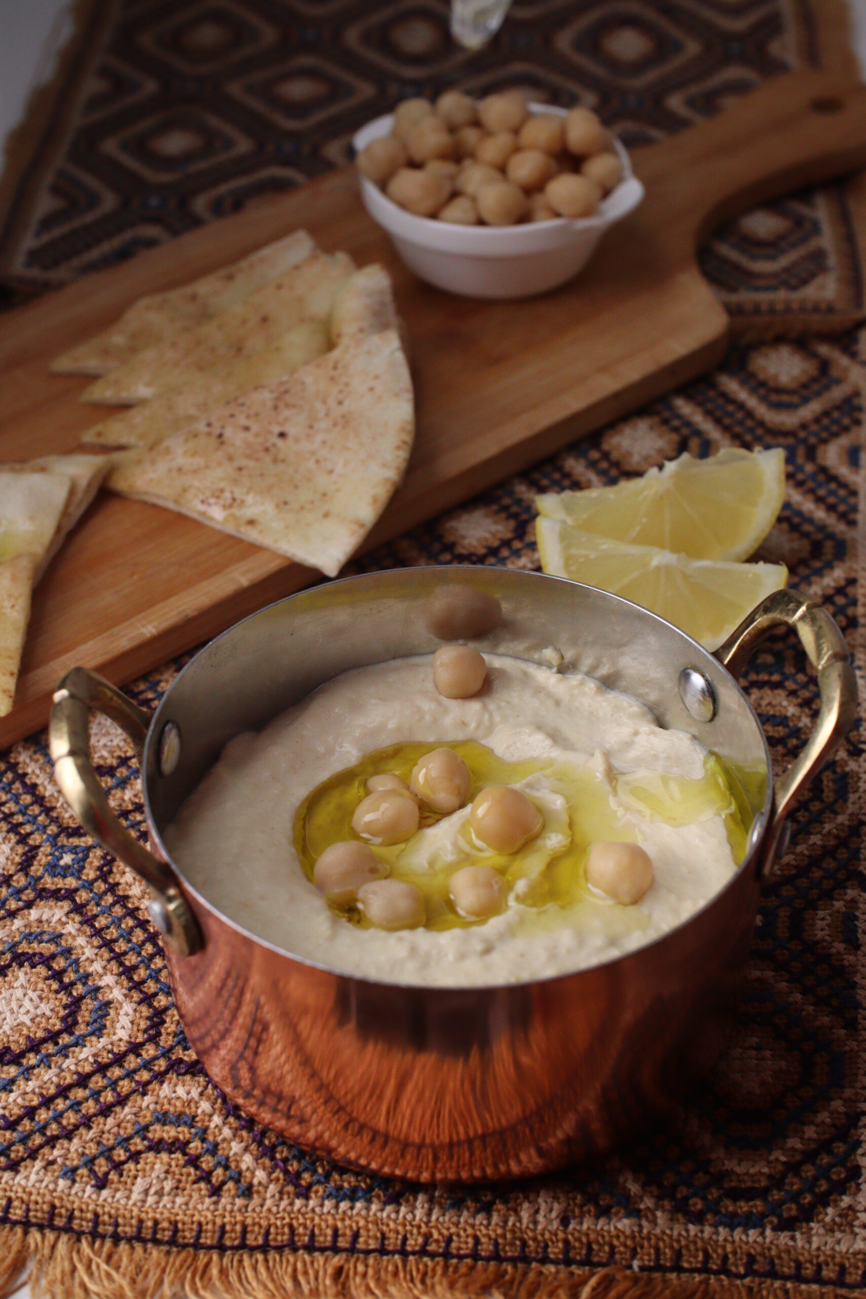 Middle Eastern dip Hummus topped with olive oil & chickpeas, served with pita bread in the background 
