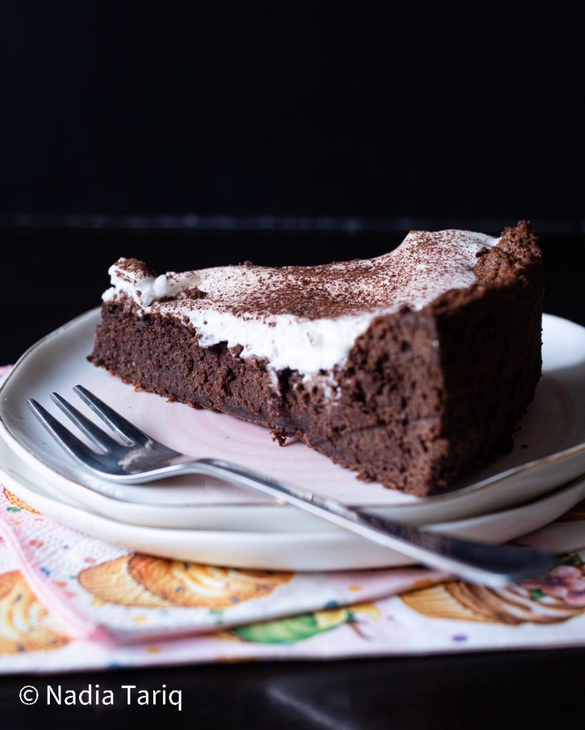 Chocolate Torte Slice with whipped cream and dusted with cocoa powder placed on pink plate with fork