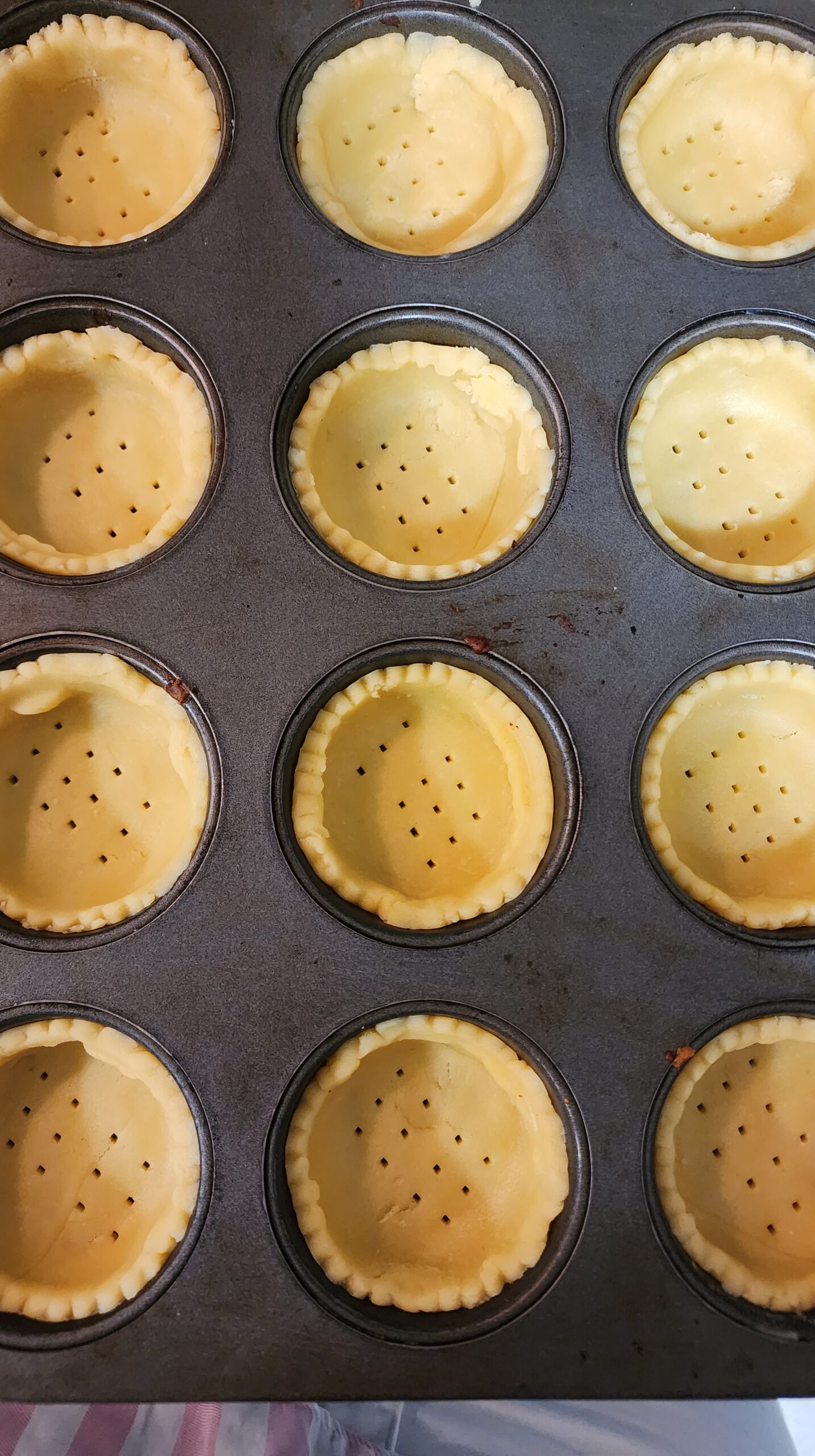 Pricked tart shells placed inside a muffin tray, ready to be baked