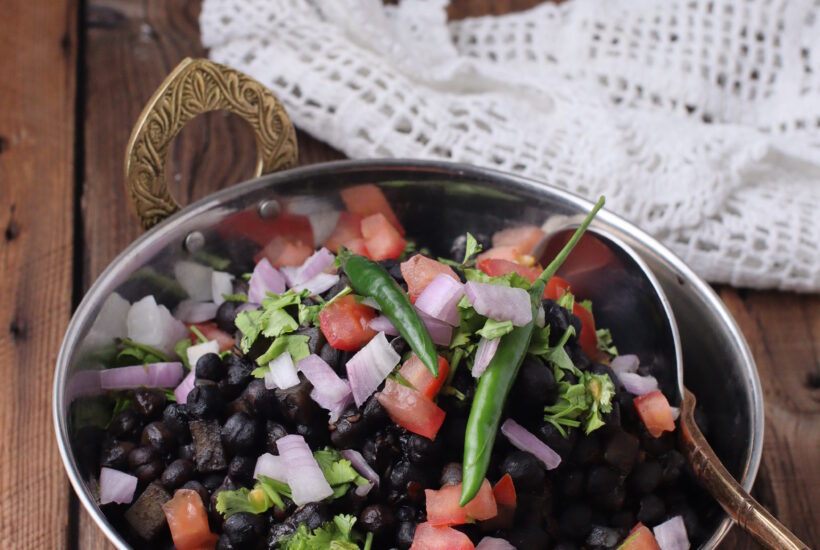 Black chickpeas/ kaalay channay served with garnish including chopped coriander, onion, tomatoes and green chili