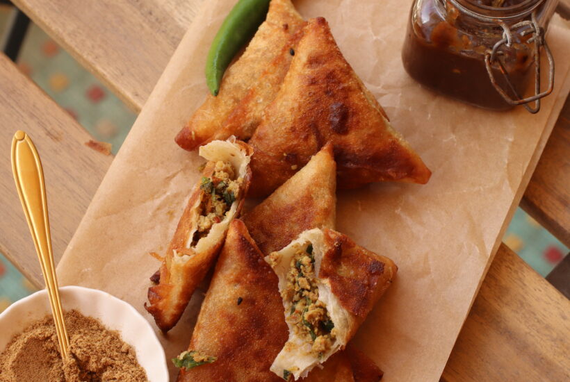 Beef keema samosas on a platter, one is broken to show the filling with a side of tamarind chutney and chaat masala