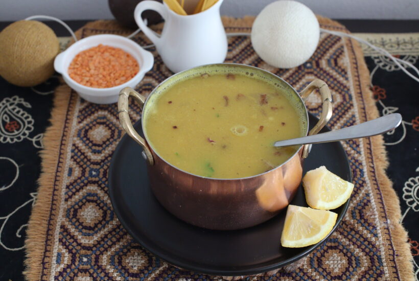 Red lentil soup in a copper bowl, served with lemon wedges